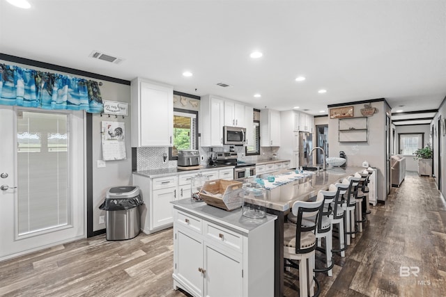 11691 Grantham Rd, Foley, AL 36535 - kitchen featuring appliances with stainless steel finishes, wood finished floors, white cabinets, backsplash, and a kitchen bar