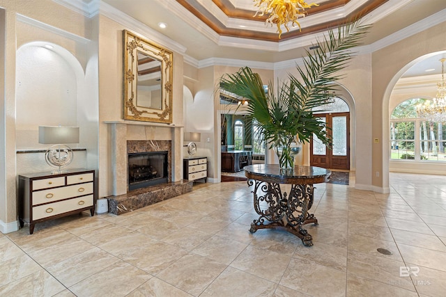 foyer entrance with a tray ceiling, arched walkways, crown molding, a fireplace, and a notable chandelier