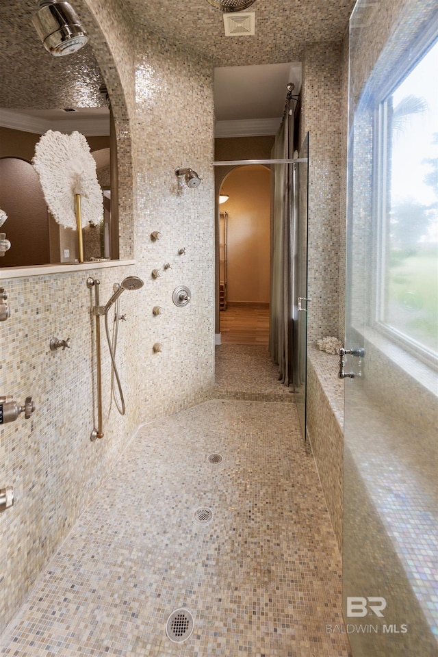 hallway with crown molding, visible vents, arched walkways, and a wealth of natural light