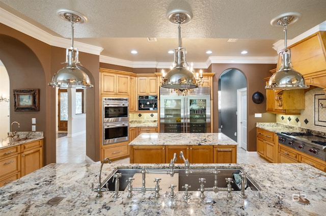 kitchen featuring appliances with stainless steel finishes, arched walkways, decorative light fixtures, and light stone countertops