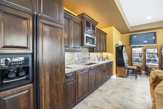 kitchen featuring glass insert cabinets, backsplash, stainless steel microwave, light stone countertops, and a sink