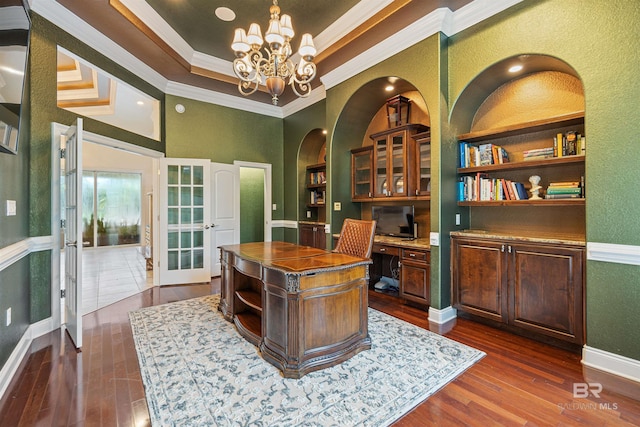 office with a raised ceiling, ornamental molding, dark wood-style flooring, an inviting chandelier, and built in desk