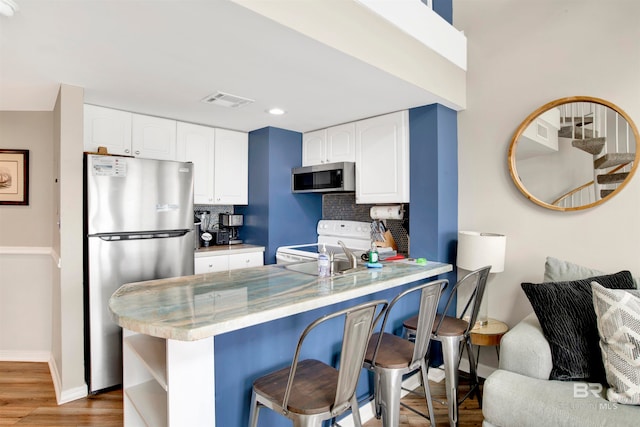 kitchen featuring wood-type flooring, kitchen peninsula, stainless steel appliances, white cabinets, and a breakfast bar area