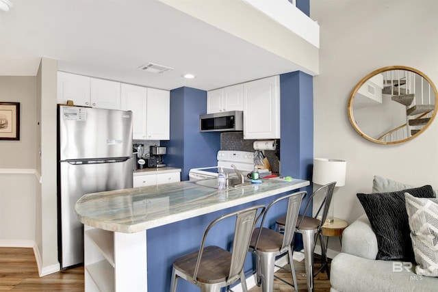 kitchen with appliances with stainless steel finishes, white cabinetry, baseboards, backsplash, and visible vents
