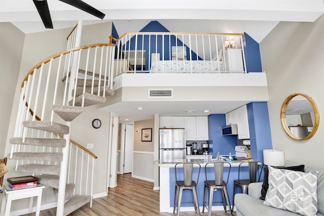 living room featuring stairs, a high ceiling, visible vents, and light wood finished floors