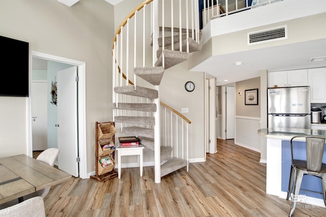 staircase featuring a towering ceiling, baseboards, wood finished floors, and visible vents