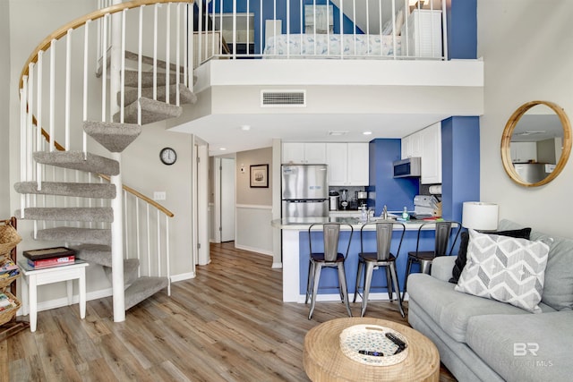 living area with light wood-style floors, baseboards, a towering ceiling, visible vents, and stairway