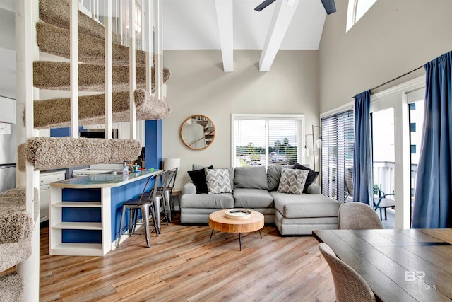 living room featuring ceiling fan, beamed ceiling, a high ceiling, and light wood-type flooring