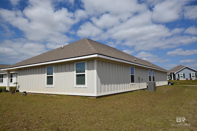 rear view of property with a lawn, cooling unit, a shingled roof, and board and batten siding