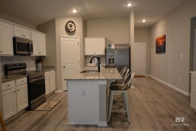 kitchen featuring a center island with sink, light wood finished floors, a sink, stainless steel appliances, and white cabinetry