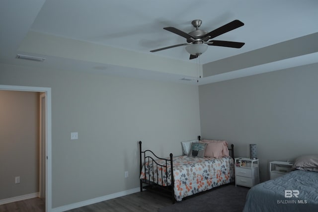 bedroom featuring a raised ceiling, wood finished floors, baseboards, and visible vents