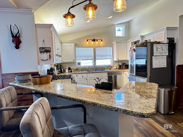 kitchen featuring lofted ceiling, appliances with stainless steel finishes, a sink, a peninsula, and a kitchen bar