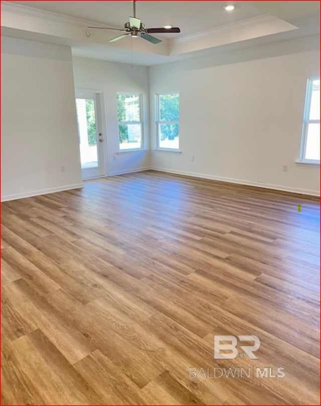 unfurnished room featuring a tray ceiling, ceiling fan, ornamental molding, and light wood-type flooring