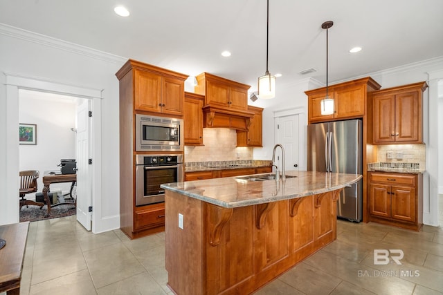 kitchen featuring a kitchen island with sink, stainless steel appliances, sink, light stone countertops, and pendant lighting