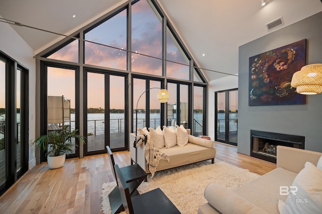 living room featuring floor to ceiling windows, french doors, light hardwood / wood-style floors, and a water view