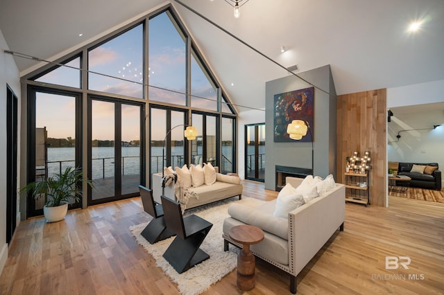 living room with a wall of windows, high vaulted ceiling, light hardwood / wood-style floors, and a water view