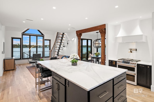 kitchen featuring a water view, custom exhaust hood, range with two ovens, light stone countertops, and a kitchen island