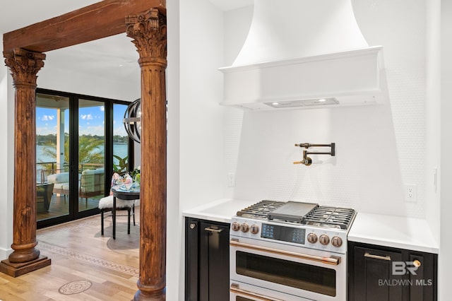 kitchen featuring french doors, custom range hood, light hardwood / wood-style floors, tasteful backsplash, and stainless steel gas range oven