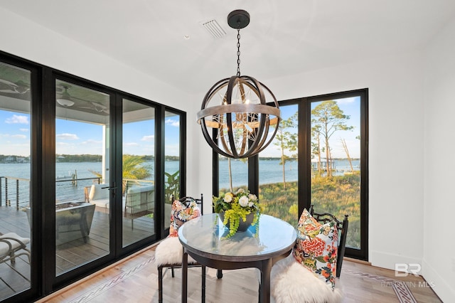 dining area featuring light hardwood / wood-style flooring, a water view, and a chandelier