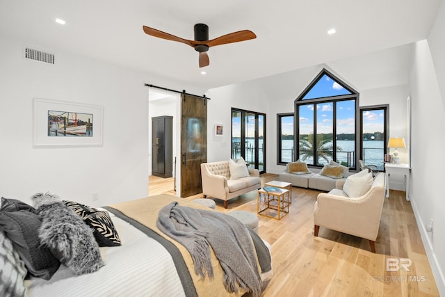 bedroom featuring light wood-type flooring, a water view, a barn door, and lofted ceiling