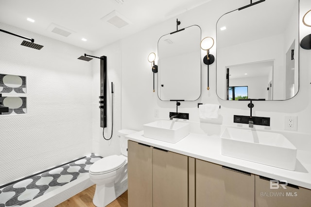 bathroom featuring toilet, vanity, hardwood / wood-style flooring, and tiled shower