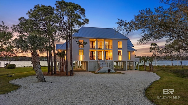 back house at dusk with a balcony, a water view, and a carport