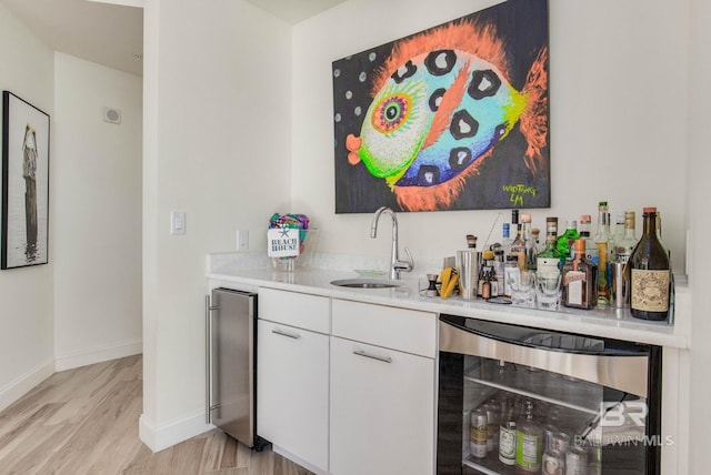 bar featuring white cabinets, beverage cooler, light wood-type flooring, and sink