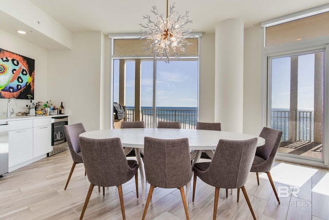 dining area featuring wine cooler, light hardwood / wood-style floors, sink, an inviting chandelier, and a water view