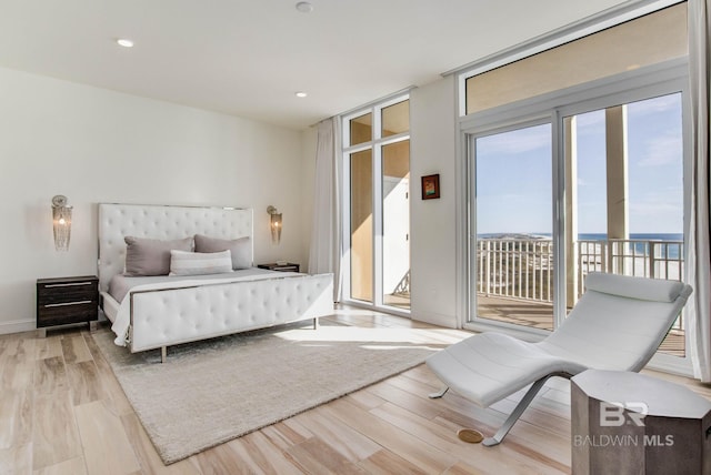 bedroom featuring light wood-type flooring, a water view, access to exterior, and expansive windows