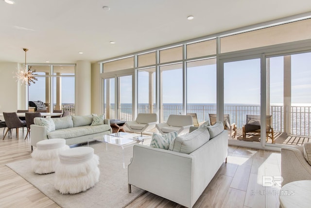 living room featuring light wood-type flooring, a water view, expansive windows, and a notable chandelier