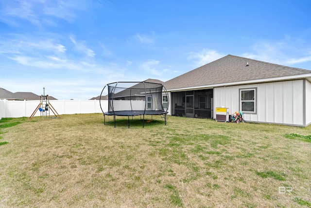 back of house featuring a sunroom, a fenced backyard, roof with shingles, a trampoline, and a yard