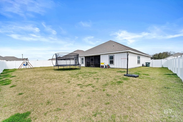 back of house with a trampoline, a fenced backyard, and a yard