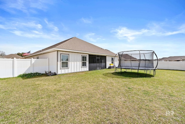 rear view of house featuring a trampoline, a sunroom, a fenced backyard, and a lawn