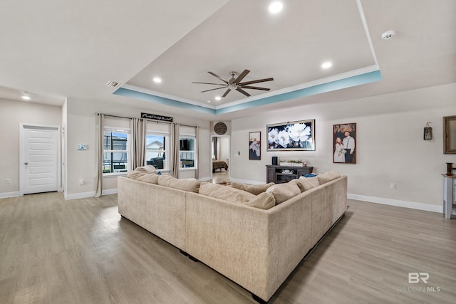 living area with light wood-type flooring, baseboards, visible vents, and a raised ceiling