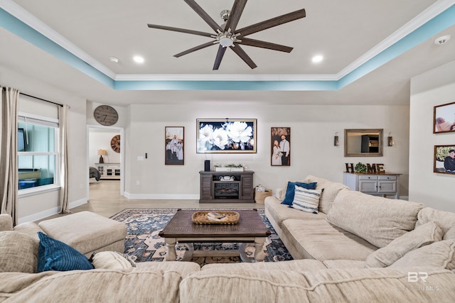 living room featuring ornamental molding, a tray ceiling, a fireplace, and baseboards