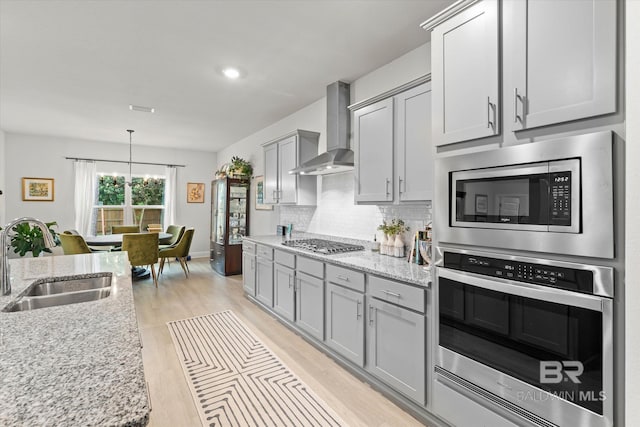 kitchen with wall chimney exhaust hood, a sink, stainless steel appliances, gray cabinets, and light wood-style flooring
