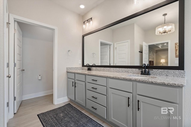 bathroom featuring wood finished floors, double vanity, baseboards, and a chandelier
