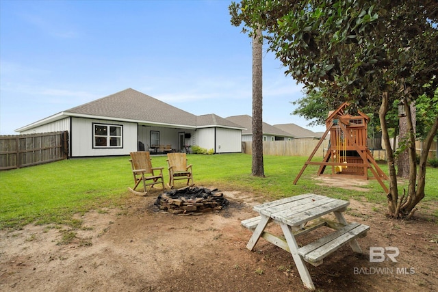back of property with a fire pit, a playground, and a shingled roof