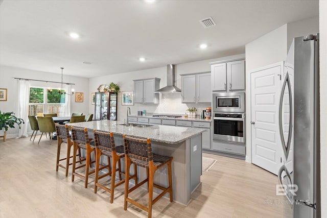 kitchen featuring stainless steel appliances, wall chimney range hood, gray cabinets, a sink, and light wood-style flooring