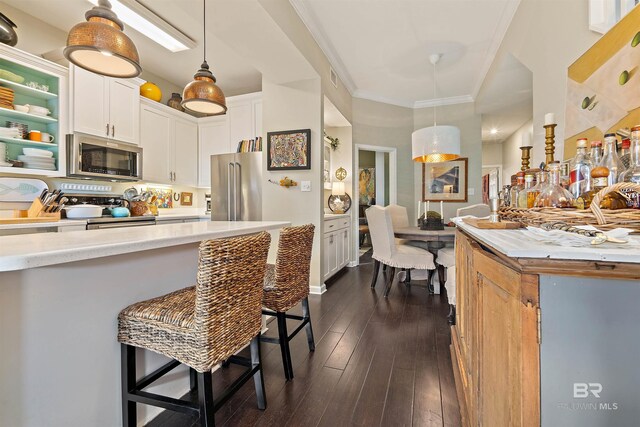 kitchen featuring a breakfast bar, pendant lighting, stainless steel appliances, light countertops, and white cabinets