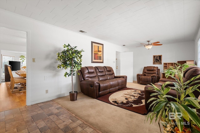 living room with ceiling fan, visible vents, stone tile flooring, and baseboards