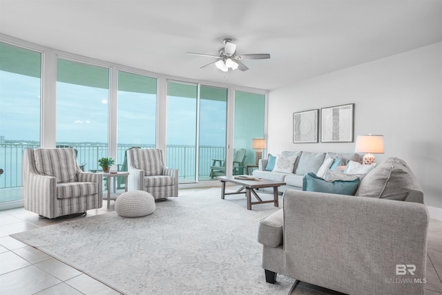 living room with ceiling fan, light tile patterned flooring, a water view, and a wall of windows