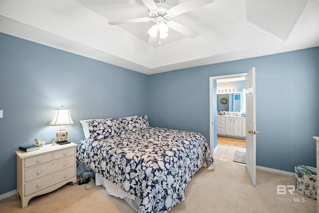 bedroom featuring light carpet, a raised ceiling, connected bathroom, and baseboards