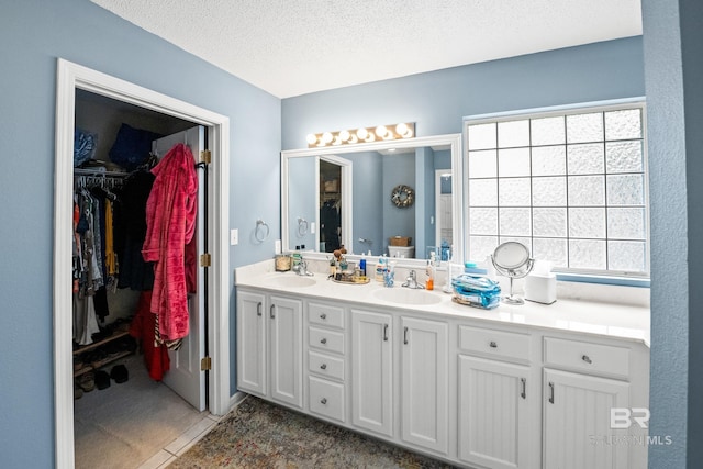 full bath featuring a walk in closet, a sink, a textured ceiling, and double vanity