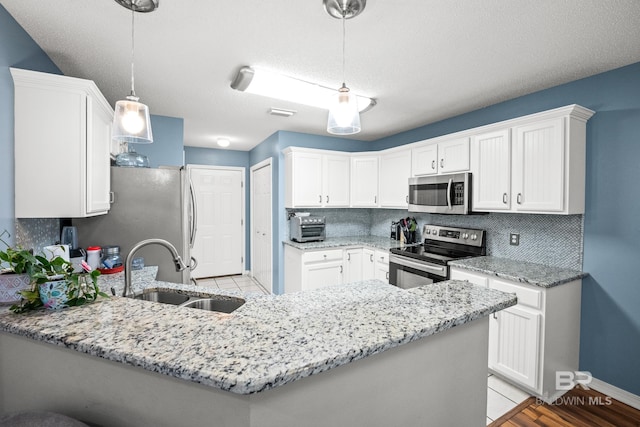 kitchen with a peninsula, white cabinetry, appliances with stainless steel finishes, and a sink