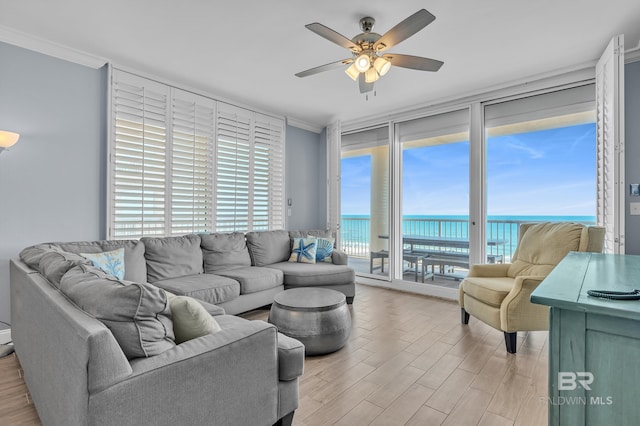 living area with floor to ceiling windows, healthy amount of natural light, ornamental molding, a ceiling fan, and a water view
