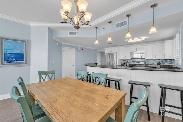 dining room with light wood-style floors, ornamental molding, a chandelier, and baseboards