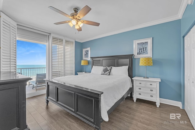 bedroom with crown molding, wood finished floors, baseboards, a ceiling fan, and a water view