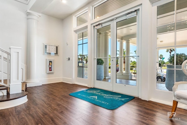 doorway featuring decorative columns, wood finished floors, baseboards, and a towering ceiling
