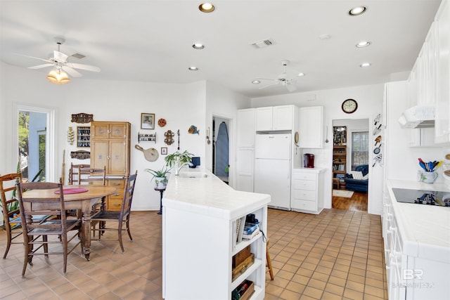 kitchen with black electric stovetop, a sink, visible vents, tile counters, and freestanding refrigerator